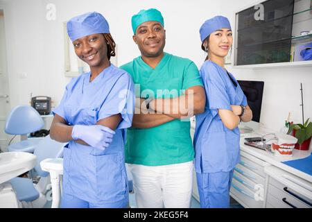Three dentists pose smiling in a dental office, work in the health sector. Stock Photo