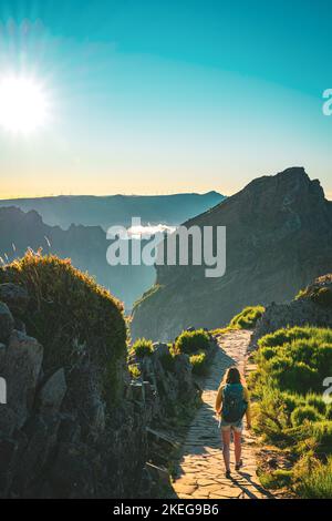 Description: Sporty woman with backpack walking along super scenic hike trail on Pico do Ariero in the evening sun. Verade do Pico Ruivo, Madeira Isla Stock Photo