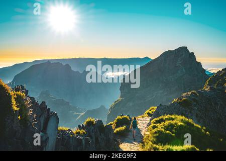 Description: Sporty woman with backpack walking along super scenic hike trail on Pico do Ariero in the evening sun. Verade do Pico Ruivo, Madeira Isla Stock Photo