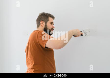 Man smoothes wall surface with a wall grinder. Male grind a white plaster wall - renovation and redecoration concept Stock Photo