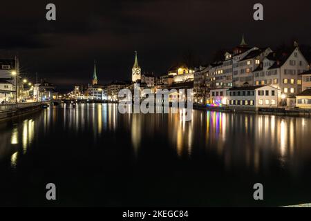 A panoramic shot of the city of Zurich at night with buildings around the lake and lights reflecting in the water Stock Photo