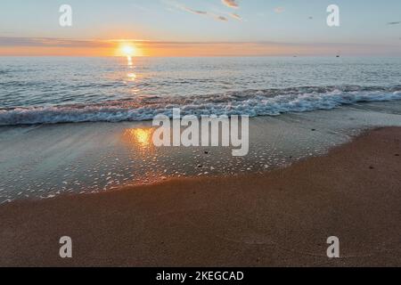Sunrise on the seashore on the Italian Riviera. Sandy beach and waves reflecting the sunlight in the foreground. Vacation travel holiday banner, summer mood. The Ligurian Sea, Italy Stock Photo