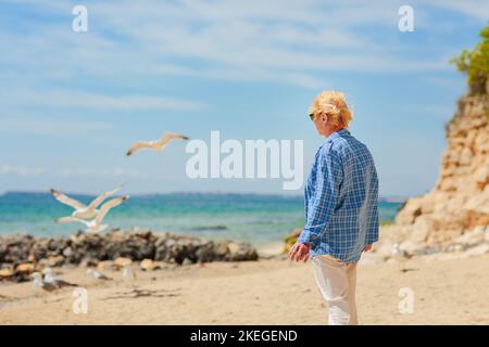 Elderly woman standing on the beach and looking into the distance Stock Photo