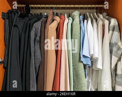 Variety of casual teenage girl clothes of different colors on hangers in wooden wardrobe Stock Photo