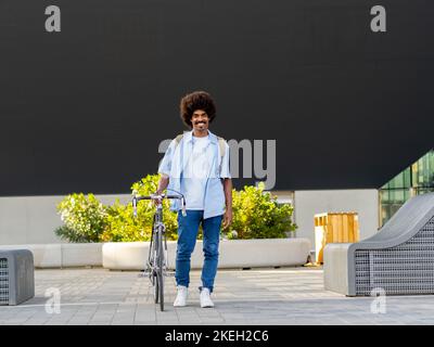 Smiling young african american man with afro hair in a financial district with a bicycle looking at camera Stock Photo