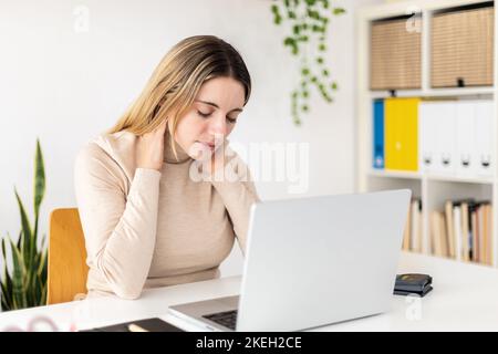 Young business woman suffering neck pain working on laptop at home Stock Photo