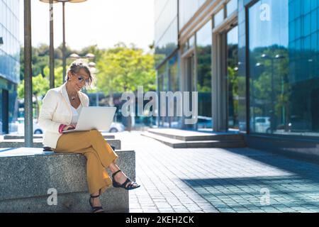 Happy attractive business woman middle-aged working smiling with laptop in front of a modern building Stock Photo