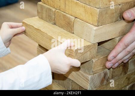 Board game Jenga Tower made of wooden blocks. A tower of unevenly shifted wooden beams. A lesson for agility, logic and coordination. Home entertainme Stock Photo