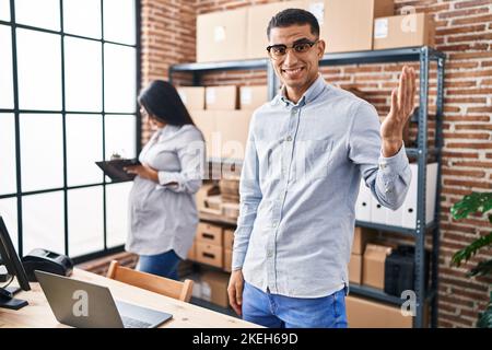 Young hispanic couple expecting a baby working at small business ecommerce celebrating achievement with happy smile and winner expression with raised Stock Photo