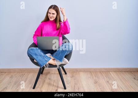Young hispanic girl working using computer laptop angry and mad raising fist frustrated and furious while shouting with anger. rage and aggressive con Stock Photo