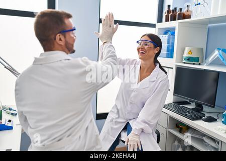 Man and woman scientist partners high five with hands raised up at laboratory Stock Photo