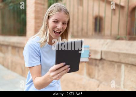 Young blonde woman using touchpad drinking coffee at street Stock Photo