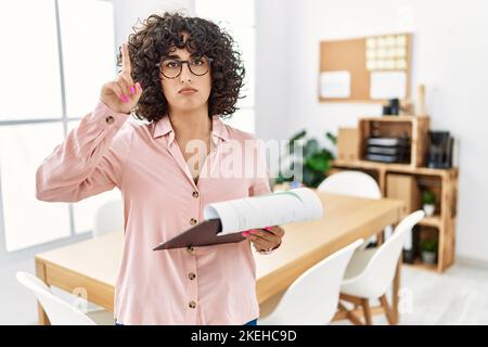 Young middle eastern woman wearing business style at office pointing up looking sad and upset, indicating direction with fingers, unhappy and depresse Stock Photo