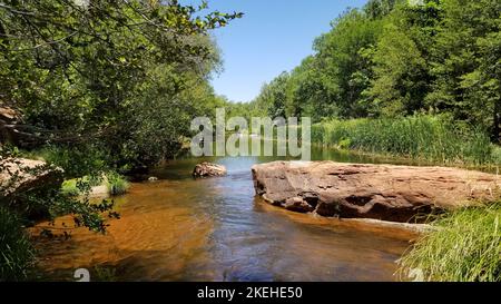 A river with rocks and green trees around in the daytime with a clear blue sky, Oak Creek, Sedona, Arizona Stock Photo