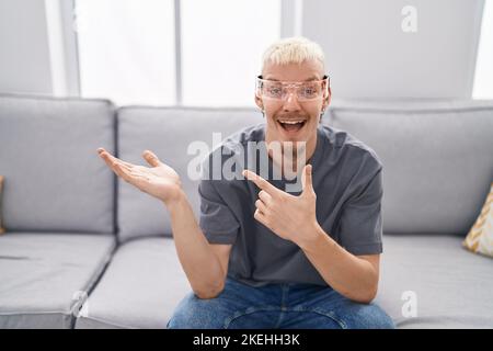 Young caucasian man wearing virtual reality glasses amazed and smiling to the camera while presenting with hand and pointing with finger. Stock Photo