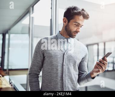 Checking his calendar. a handsome young businessman looking at his cellphone while standing in the office. Stock Photo