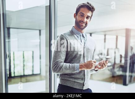 Accessing my calendar on the move. Cropped portrait of a handsome young businessman looking at his cellphone while standing in the office. Stock Photo