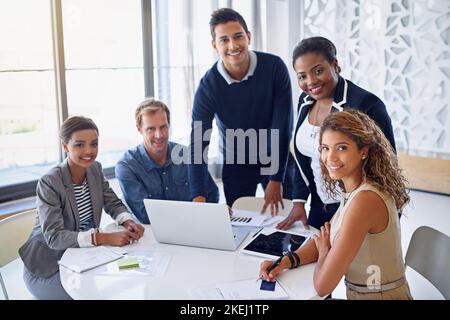 Your companys dream team. Portrait of a group of coworkers working together on a laptop in an office. Stock Photo