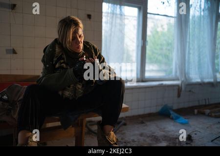 Special female soldier after the fight sitting in ruined building smoking cigarette staring at the camera. War, post apocalypse Stock Photo