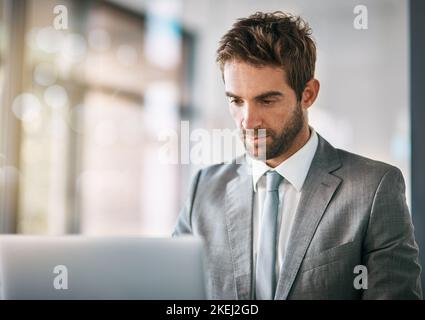 The focus that gets it done. a handsome young businessman using a laptop in a modern office. Stock Photo