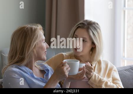Woman and middle-aged mother holding mugs, enjoy talk Stock Photo