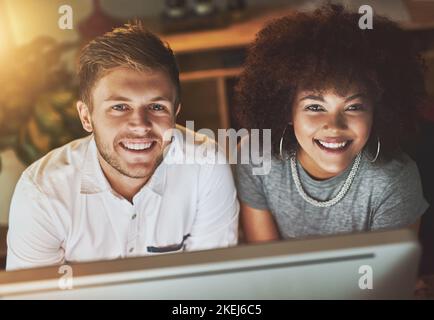 Putting our heads together. two young designers working together on a computer while looking at the camera in the office. Stock Photo