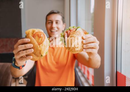 Happy man eating two hamburger or sandwich with an appetite in a fast food cafe. Stock Photo