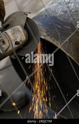 Shallow depth of field (selective focus) details with a worker using an angle grinder on an industrial metallic pipeline. Stock Photo