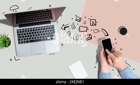 A person sends various files from a smartphone to a laptop using wireless technology. Stock Photo