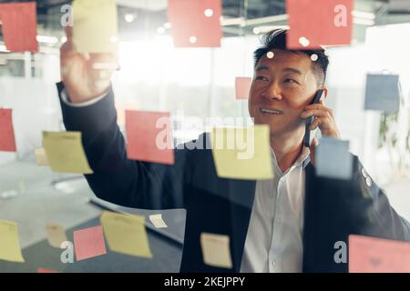 Businessman writing on sticky notes on glass wall while working in modern office Stock Photo