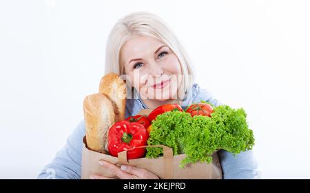 Happy woman with blond hair and beautiful smile holds products from the store in paper bag of vegetables in her hands for a healthy diet with Stock Photo