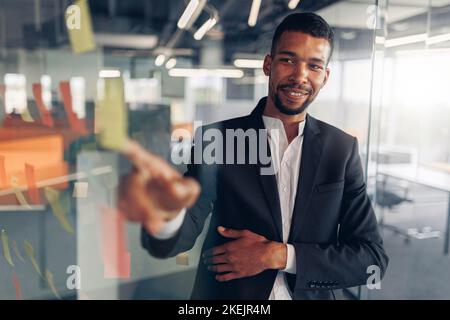 Businessman showing on sticky notes on glass wall while working in modern office Stock Photo