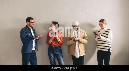 Happy businesspeople chatting and using their smartphones while standing in a waiting area. Group of shortlisted candidates prepping for a job intervi Stock Photo