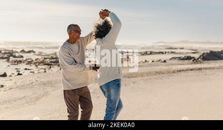 Romantic elderly couple dancing together by the beach. Happy mature couple having a good time next to the ocean. Cheerful senior couple enjoying their Stock Photo