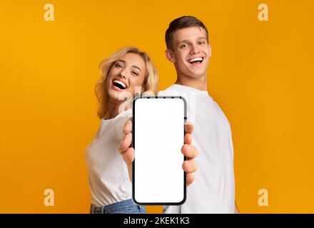 Laughing happy young caucasian male and female with open mouth show smartphone with empty screen Stock Photo