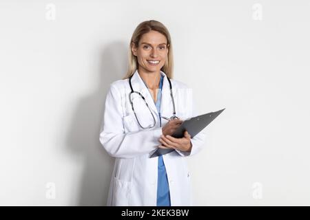 Medical Services. Portrait Of Beautiful Smiling Doctor Lady In Uniform Holding Clipboard Stock Photo