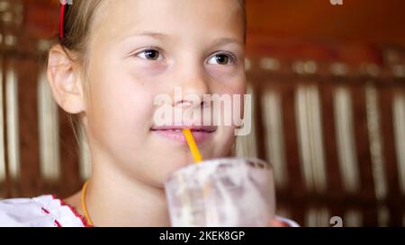 happy smiling teen girl child drinks a milkshake in cafe. she is dressed in Ukrainian national clothes, embroidery, vishivanka. High quality photo Stock Photo