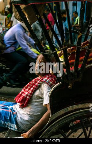 Kolkata, India - July 9, 2022: A hand pulled Rickshaw Wala relaxing and looking into the camera. Selective focus with background blur. Stock Photo