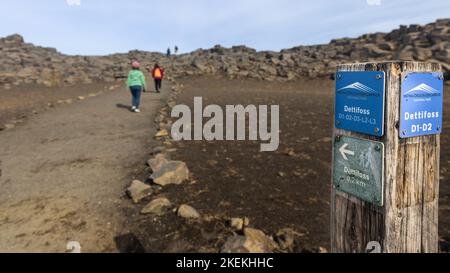 Direction post to Dettifoss waterfall trail, Iceland, with hikers at background Stock Photo