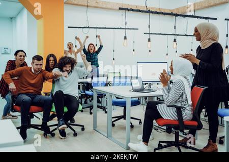 Team building and office fun. Young cheerful businesspeople in smart casual wear having fun while racing on office chairs and smiling. Stock Photo