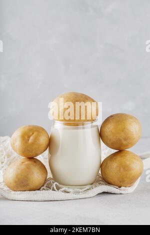 Alternative potato milk in glass and potatoes. Alternative non dairy drink and string bag. Vegan potato milk and sustainable lifestyle concept Stock Photo