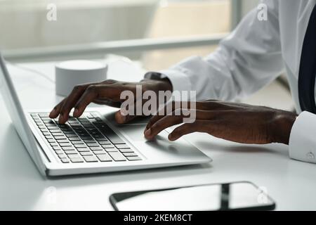 Close-up of African American businessman typing on laptop and doing his online work at table at office Stock Photo