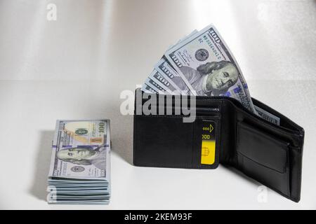 Black leather wallet with dollars on a white table. Stack of one hundred dollar bills american dollars Stock Photo