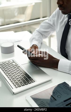 Close-up of African American businessman having online communication on smartphone while working on computer at office Stock Photo