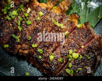 Close-up Australian sliced medium rare wagyu grilled beef steak top with sliced spring onion on glass plate on dark background, japanese style. Austra Stock Photo