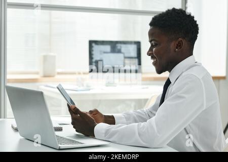 Young African American businessman using wireless devices at his workplace at office, he working online on digital tablet Stock Photo