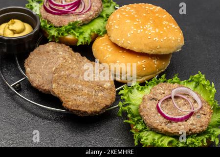 Round buns, beef burger with greens and chopped onions. Mustard in bowl. Black background. Stock Photo