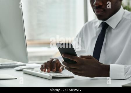 Close-up of young businessman using his smartphone while working on computer at table at office Stock Photo