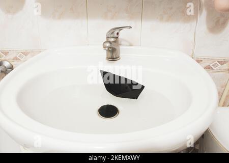 Children's paper boat floats in the sink in the bathroom at home Stock Photo