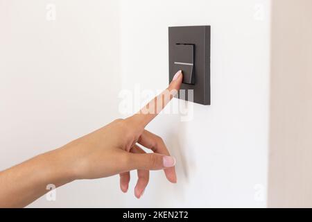 Close up of young woman's hand pressing the light switch button Stock Photo